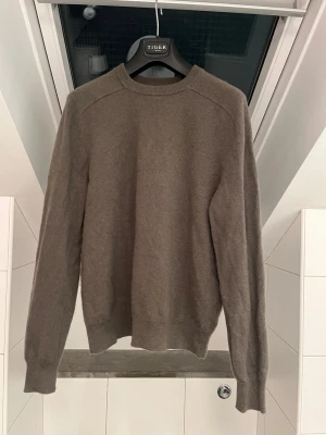 Brun stickad tröja från Tiger - Snygg brun stickad tröja från Tiger med rund hals och långa ärmar. Enkel och stilren design som passar perfekt till jeans eller chinos. Mjuk och skön kvalitet som håller dig varm under kyliga dagar.