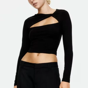 Svart croppad topp - Säljer en svart croppad topp med lång ärm och cool cut-out detalj över bröstet. Toppen har en tight passform. 