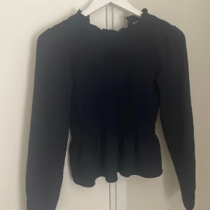 Mörkblå långärmad blus med rynk - Säljer en mörkblå blus med lång ärm och rynkdetaljer över hela livet. Blusen har en lätt volang vid halsringningen och är figursydd i midjan för en snygg siluett. Perfekt för dig som gillar stilrena och trendiga plagg.sitter tajt