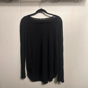 Svart långärmad tröja med rund hals - En enkel svart långärmad tröja med rundad hals och rak passform. Perfekt att matcha med jeans eller under en jacka. Materialet känns mjukt och lätt, vilket gör den skön att bära hela dagen.