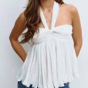 Vit plisserad halterneck linnetopp - Supersnygg vit linnetopp med plisserat tyg och halterneck som knyts i nacken. Toppen har en twistad detalj framtill och är ärmlös med luftig, flowy passform. Helt ny och oanvänd utan prislapp💞ordinarie pris 349kr, snabb affär kan pris diskuteras!☺️