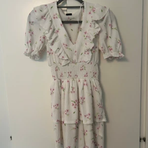 Vit blommig volangklänning - Supersöt vit klänning med rosa blommor och gröna blad från Gina tricot i storlek XXS säljes för 250kr. Mycket fint skick. 