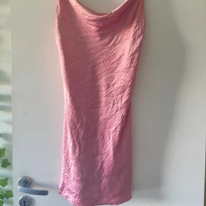 Rosa satinklänning från Gina Tricot - Säljer en rosa satinklänning från Gina Tricot med smala axelband och snygg draperad urringning. Klänningen är figurnära och har en mjuk glansig yta som ger en lyxig känsla. Perfekt för dig som vill sticka ut med en feminin look. Normal i storlek. Den går ungefär till mitten av låren. Tyvärr lite skadad i tyget, se bild. Inget som stör användandet.🌸
