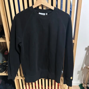 Carhartt svart sweatshirt, storlek Xs -  Svart sweatshirt med rund halsringning och långa raglanärmar. Tröjan har en ribbstickad mudd nedtill och vid ärmslut. En broderad Carhartt-logga finns på vänster ärm.