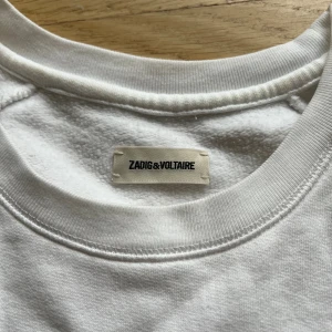 Vit sweatshirt Zadig & Voltaire - Vit sweatshirt från Zadig & Voltaire med röd metallic logga framtill. rund halsringning och långa ärmar. Mjuk insida och relaxed fit. Tillverkad i bomull 