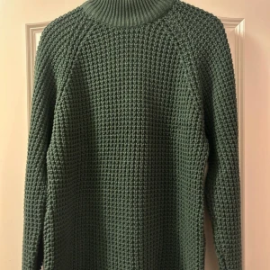 Grön stickad polotröja - Mysig mörkgrön stickad polotröja med grov struktur och hög krage. Tröjan har lång ärm och en loose fit som ger en avslappnad vibe. 