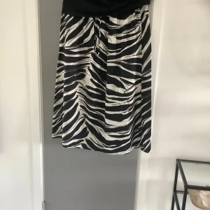 Zebramönstrad svartvit kjol - Snygg kjol med zebramönster i svart och vitt. Kjolen har resår i midjan för en bekväm passform och är i en luftig, lätt form som slutar strax ovanför knäna. Perfekt för dig som vill sticka ut med ett djurmönster.