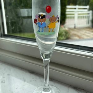 Lasse Åberg champagne glas -  ett champagneglas med en charmig illustration av två möss, en med blombukett och en med ballong. Glaset är signerat av Lars Åberg.