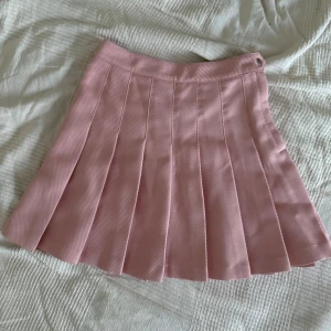 Rosa plisserad kjol från H&M - Supersöt rosa plisserad kjol från H&M i kort modell. Kjolen har bred linning och tydliga veck som ger en klassisk preppy look.  Mycket bra skick, knappt använd. 