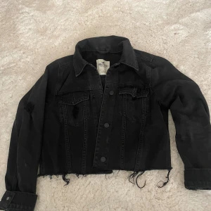 Svart croppad jeansjacka Hollister  - Svart croppad jeansjacka från Hollister med slitna detaljer i storlek S