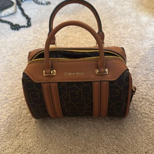 Calvin Klein brun och svart handväska - Säljer en Calvin klein väska då den inte kommer till användning. Aldrig använd och har inga effekter. Köpt i usa för runt 110$. Tveka inte vid frågor