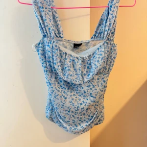 Blommig blå söt topp  - Supersöt  i ljusblått med små blå blommor över hela.  har breda axelband och en lätt rynkad detalj vid bysten. Perfekt för Materialet känns mjukt och stretchigt.