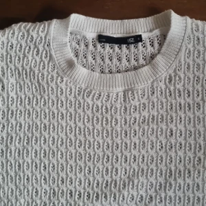 Vit stickad tröja från lager 157, S - Vit stickad tröja från laher 157 i storlek S. Tröjan har ett luftigt, hålmönstrat stickat material och ribbade muddar vid hals och ärmslut. Perfekt för lager-på-lager och ger en fräsch vibe till din outfit.