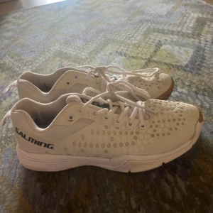 Vita Salming sneakers med bikakemönster - Säljer ett par vita Salming sneakers med bikakemönstrad mesh och detaljer i syntet. Skorna har snörning och en platt sula med gummidetaljer framtill. Perfekta för dig som gillar sportig stil och vill ha något lätt och luftigt på fötterna. jag har använt de när jag spelar handboll och jag är tjej men skulle säga unisex 