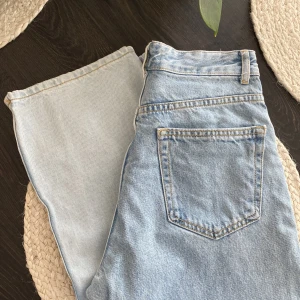 Tvåfärgade jeans från Pull&Bear - Unika tvåfärgade jeans från Pull&Bear i storlek 36. Ena benet är ljusblått och det andra är klassiskt blått, vilket ger en cool kontrast. Jeansen har hög midja, raka ben och klassiska fickor både fram och bak. Tillverkade i bomullsdenim med snygga sömmar.