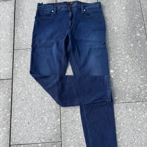 Mörkblå jeans från Alberto - Snygga mörkblå jeans från Alberto med klassisk femficksdesign och kontrastsömmar i orange. Jeansen har rak passform och är tillverkade i mjukt bomullsmaterial med stretch för extra komfort. Perfekta för dig som gillar stilrena och bekväma jeans.