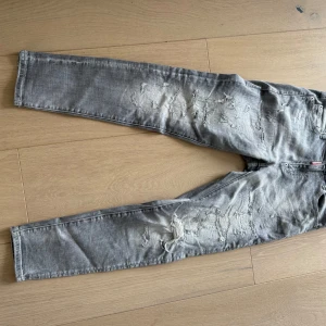 Grå slitna jeans från Dsquared2 - Säljer ett par grå jeans från Dsquared2 med snygga slitningar och distressed detaljer. Modellen är slim fit och byxorna har klassisk femficksdesign. Jeansen är tillverkade i bomull och har en cool, tvättad look med Dsquared2-logga vid gylfen.