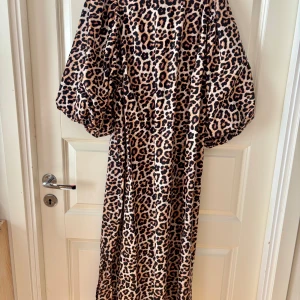 Leopardmönstrad långklänning med puffärm - Säljer en maxad långklänning med leopardmönster och stora puffärmar. Klänningen har loose passform och är tillverkad i ett glansigt, mjukt material som ger en lyxig känsla. Perfekt för dig som vill sticka ut och älskar djurmönster.