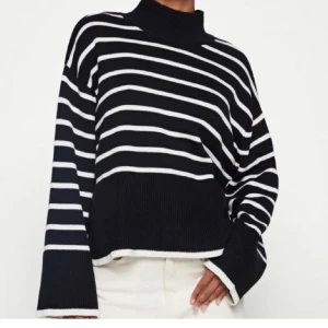 Randig svartvit stickad polotröja - Snygg stickad polotröja i svart med vita ränder. Tröjan har en hög krage, långa ärmar och en loose passform. Perfekt för dig som gillar en avslappnad men trendig stil.