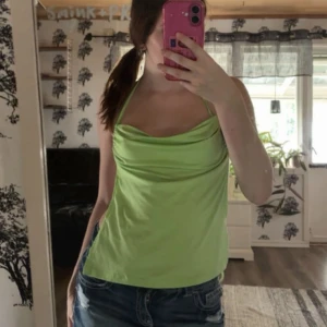 Ljusgrön halterneck linnetopp - Säljer en ljusgrön halterneck topp med snygg drapering framtill och knyt i nacken och ryggen. Toppen är ärmlös och har en croppad passform som passar perfekt till jeans eller kjol. Materialet känns mjukt och svalt, perfekt för varma dagar.