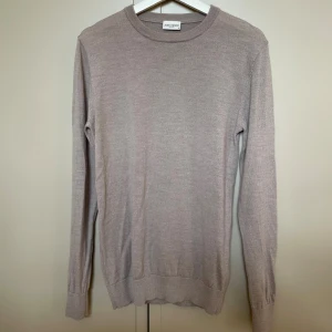 Beige stickad tröja från John Henric i merinoull  - Snygg beige stickad tröja från John Henric med rund hals och ribbade muddar vid ärmslut och nederkant. Tröjan har en clean och klassisk look, perfekt för dig som gillar stilrena plagg. Materialet är i mjuk merinoull.