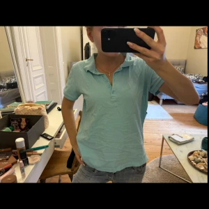 Ljusblå piké topp med krage - Säljer en ljusblå piké topp med klassisk krage och knappslå framtill. T-shirten har korta ärmar och är gjord i mjuk bomull, perfekt för en chill och sportig look. Enkel att matcha med jeans eller shorts.🩵