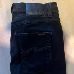 Nudie Jeans Lean Dean svarta jeans - Svarta Nudie Jeans Lean Dean med smal passform och klassisk femficksdesign. Jeansen är tillverkade i 99% ekologisk bomull och 1% elastan för extra stretch. Snygga detaljer med svarta sömmar och diskret logga på bakfickan.