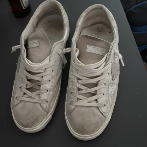 Philippe Model vita sneakers i mocka - Säljer ett par vita Philippe Model sneakers i mocka och skinn med klassisk låg profil. Skorna har snörning, rund tå och platt sula. Sidan pryds av märkets sköldlogga och detaljer i silver. Kommer med originalkartong och dustbag.Ganska bra skick skulle jag själv säga har haft dessa i 2månader men de är för små för mig och det är därför jag säljer de