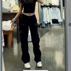 Svarta cargopants med fickor - Säljer ett par svarta cargopants med flera fickor på benen och avslappnad passform. Byxorna har raka ben och knappar vid fickorna. Från hollsiter och är i storlek 00-R som motsvarar S/34 ish 