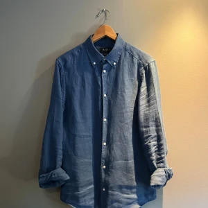 Blå linneskjorta från Riley - Snygg blå skjorta från Riley i regular fit, tillverkad i linne. Skjortan har klassisk krage med knappar och vita knappar längs hela framsidan. Använd 2-3 gånger endast nu i sommras. I stolek S.