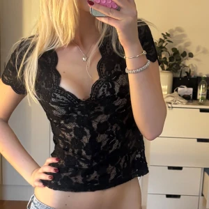 Festtopp spets!! - Säljer en svart, genombruten spetsblus med v-ringning och korta ärmar. Toppen är croppad och har ett blommigt spetsmönster som ger en snygg och feminin look. Perfekt att styla med jeans eller kjol för en trendig outfit.