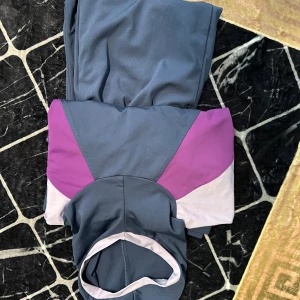 Navy simkläder från Speedo - Navy heltäckt simkläder från Speedo. Byxorna har resår i midjan och är perfekta för simträning. Matchande överdel har lila och ljusrosa detaljer med luva för att täcka håret.