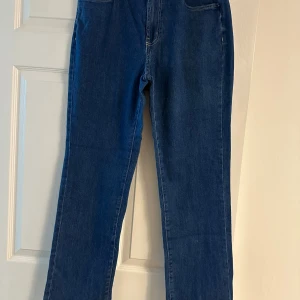 Blå raka jeans från SHEASE - Klassiska blå jeans från SHEASE med raka ben och hög midja. Jeansen har fem fickor, synliga kontrastsömmar och en snygg läderpatch bak i midjan. De ger en tidlös look. Perfekta för dig som gillar enkel och clean stil.