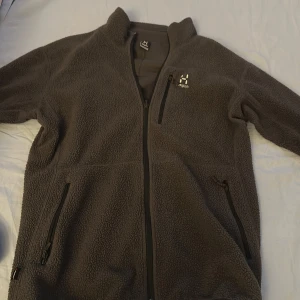 Mörkgrå hoodie Haglöfs - Mysig mörkgrå hoodie från Haglöfs med hög krage och hel dragkedja. Hoodien har tre praktiska fickor med dragkedja och broderad logga på bröstet. Perfekt för kyliga dagar och outdoor-häng. Ny skick 9,5/10!🔥