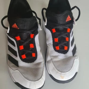 Adidas inneskor svart/vit strl 36 - Snygga fotbollsskor från Adidas i svart och vitt med klassiska tre ränder på sidan. Skorna har orange detaljer vid snörningen och är tillverkade i syntetmaterial med mesh för bra andningsförmåga. Perfekta för dig som vill sticka ut på planen.