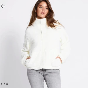 Vit teddyjacka med dragkedja - Mysig vit teddyjacka med hög krage och hel dragkedja framtill. Jackan har två stora fickor och en avslappnad passform. Perfekt för kalla dagar när du vill vara både varm och snygg.