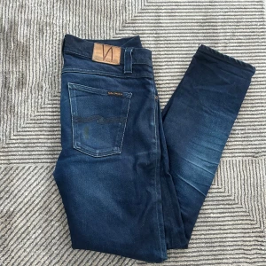 Mörkblå Nudie jeans - Snygga mörkblå skinny jeans från Nudie Jeans med klassisk femficksdesign och läderpatch bak i midjan. Jeansen har en tight passform och är tillverkade i stretchig denim för extra komfort. Perfekta för dig som gillar en stilren och modern look.