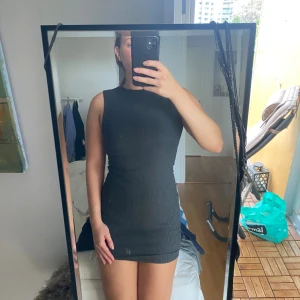 Svart ribbad ärmlös kortklänning - Säljer en svart, tight och ribbad kortklänning med ärmlös design och rund hals. Klänningen har en enkel och stilren look som sitter figurnära och är perfekt för dig som gillar minimalistisk stil.