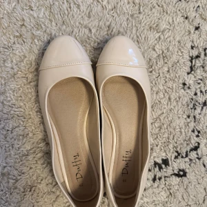 Beige/rosa ballerinaskor från Duffy - Snygga beige ballerinaskor från Duffy med rund tå och glansig finish framtill. Skorna har en klassisk och stilren design som passar till många outfits. Tillverkade i syntetmaterial och har en platt sula för extra komfort. Org pris 600kr. Bild 3 för defekt, vet ej om det bara är smuts och kan gå bort.