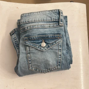 Ljusblå jeans från Gina Tricot - Snygga ljusblå jeans från Gina Tricot i klassisk femficksmodell. Jeansen har en cool ficka med lock och knapp bak, samt kontrastsömmar. Perfekta för dig som gillar en avslappnad och trendig stil.