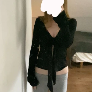 Svart omlottopp med knyt framtill - Svart långärmad omlottopp med djup v-ringning och knyt framtill. Snygg croppad passform som framhäver midjan och ger en trendig look. Nästan aldrig använd!