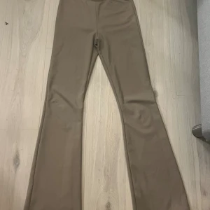 Beiga bootcut byxor med stretch - Snygga beiga byxor med bootcut-modell och stretchigt material. De har en slät midja och sitter tajt upptill med utsvängda ben. Perfekta för dig som gillar en trendig och bekväm look.