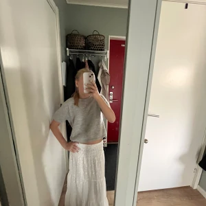 Vit långkjol med broderade detaljer - Superfin vit långkjol med broderade mönster och smock i midjan. Kjolen har en luftig och flowy känsla, perfekt för varma dagar. Snygg att styla med en enkel topp eller stickad tröja.