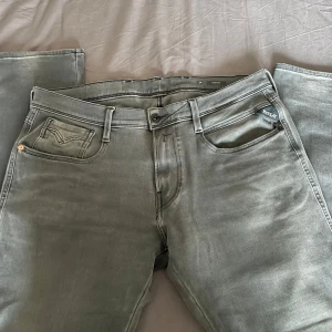 Replay Anbass grå jeans 34/30 - Snygga Replay Anbass jeans i en ljusgrå tvätt. Klassisk femficksmodell med Replay-logga på myntfickan och bakficka med diskret broderi. Jeansen har rak passform och är tillverkade i mjukt denimtyg som sitter skönt hela dagen.