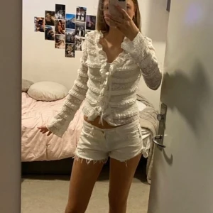 Vit spetsblus med volanger och knyt - Säljer en superfin vit blus med spets och volanger. Blusen har långa ärmar, v-ringad hals och snygg knytning framtill. Den är croppad och har romantiska detaljer som gör den extra söt. Perfekt för dig som gillar en feminin och trendig stil. Perfekt för dig som behöver en lite finare blus för en speciell dag