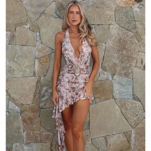 Beige omlottklänning med volang - Säljer en beige och brun kortklänning med asymmetrisk volangkant och djup v-ringning från white fox, ny pris (800 kr) . Klänningen har omlott-design, öppen rygg och knyt i nacken. Snyggt mönster och ett dekorativt bälte i midjan. Perfekt för dig som gillar att sticka ut.