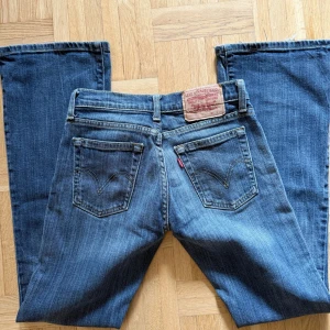 Levis 527 bootcut jeans blå - Säljer ett par klassiska Levis 527 jeans i blå denim med bootcut passform. Jeansen har låg midja, fem fickor och snygga slitningar för en cool look. Perfekta för dig som gillar en tidlös och avslappnad stil.