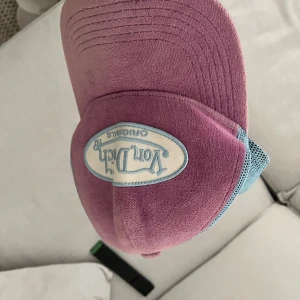 Von Dutch lila och blå keps - Säljer en ikonisk Von Dutch keps i lila med ljusblå mesh-detaljer och broderad logga framtill. Kepsen har böjd skärm och klassisk trucker-modell, perfekt för att lyfta vilken outfit som helst.