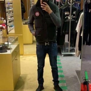 Svart dunväst från Canada Goose - Säljer en svart dunväst från Canada Goose med klassisk logga på bröstet och diskret broderad text vid fickan. Västen har hög krage, knappar och dragkedja framtill. Perfekt för lager-på-lager och riktigt snygg till jeans eller hoodie.