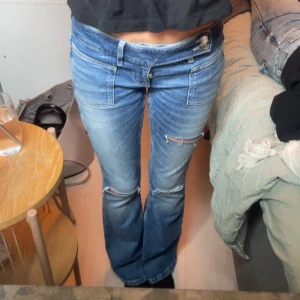 Blå bootcut jeans från gina - Säljer ett par blå bootcut jeans med låg midja och slitna detaljer vid knäna